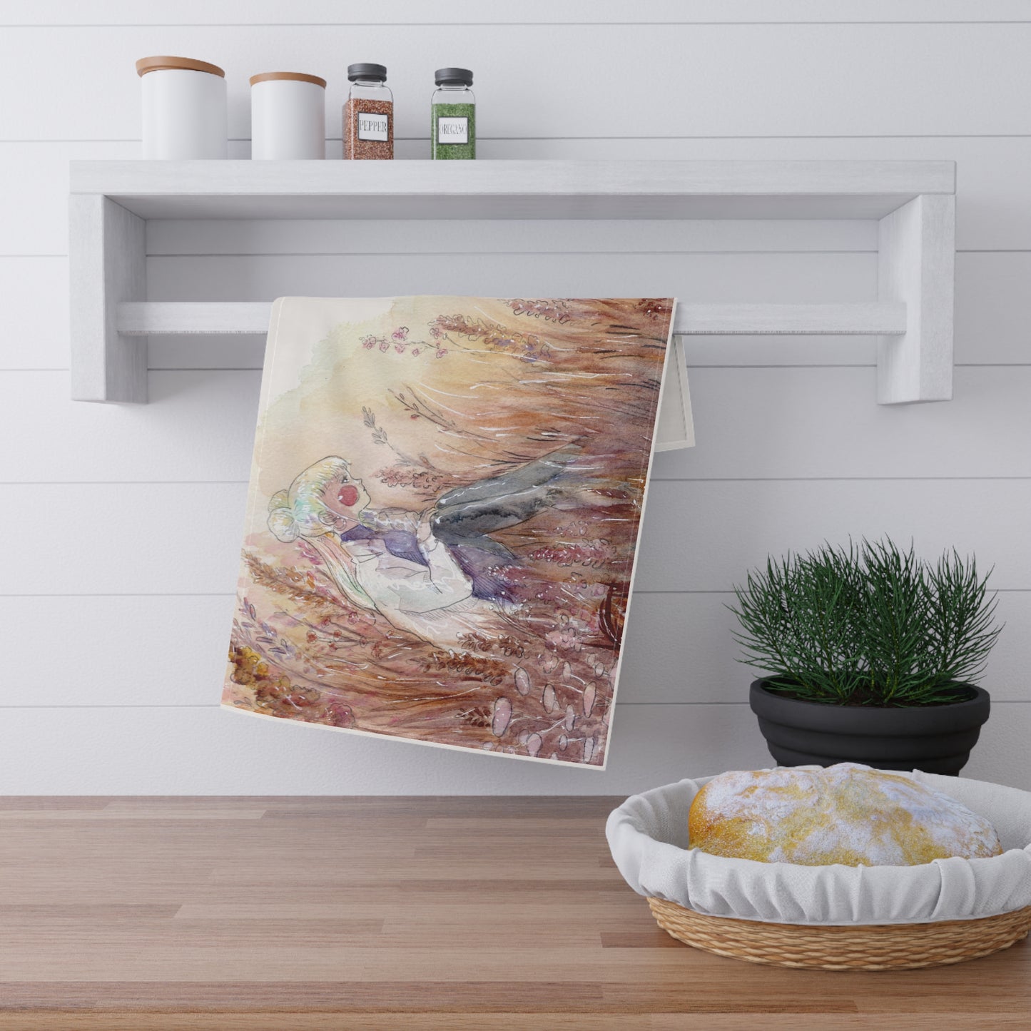 Towel with a bird design hanging on a wall above a wooden surface with a basket and plant.
